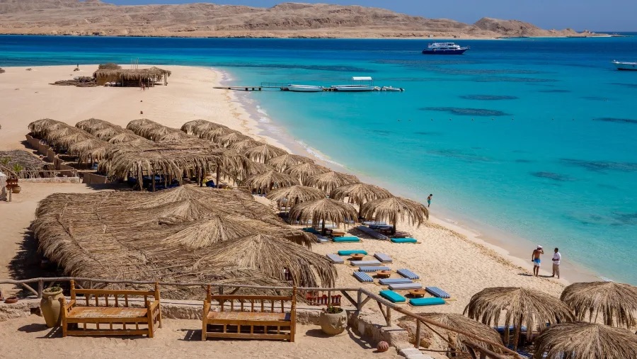 Sandstrand mit Strohschirmen und türkisblauem Wasser auf einer Insel bei Hurghada